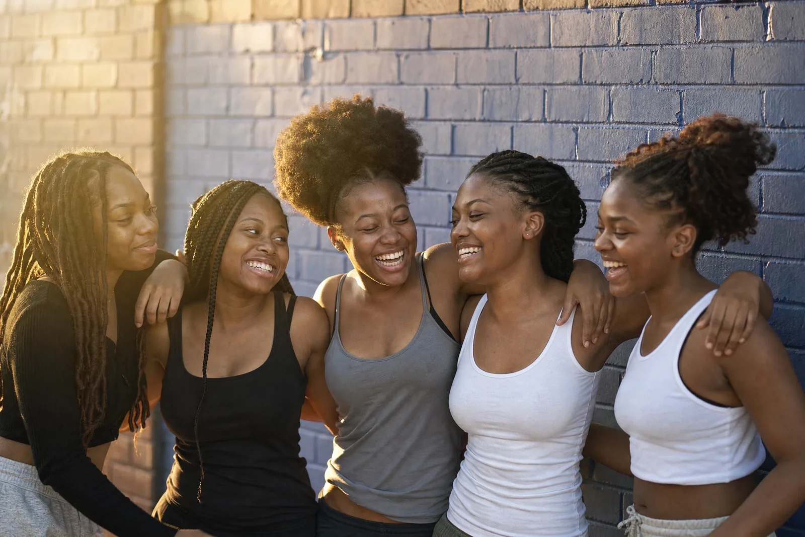Five Black teenage girls of different complexions laughing together in golden light